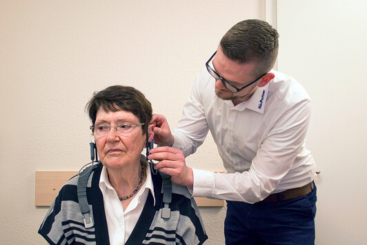 Ein Hörakustiker passt einer Seniorin im Hörtestraum moderne Hörgeräte an.